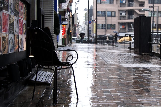 雨の中佇むベンチと街並み